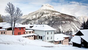 A snow-covered mountain with a prominent peak, surrounded by residential buildings with snow on their roofs. - JUFA Hotel Altaussee (Altaussee)