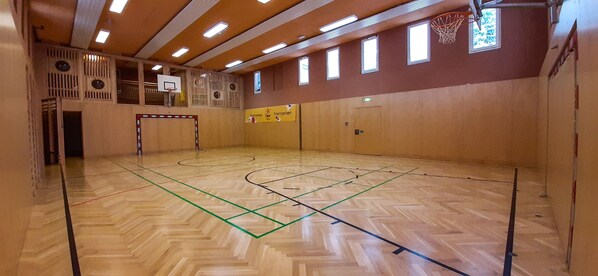 Una cancha de baloncesto cubierta con piso de madera, un aro de baloncesto y varias ventanas.