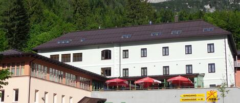 Un edificio de varios pisos con techo plano, ventanas amplias y un cartel que indica un restaurante y una terraza.