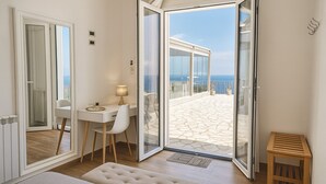 Una habitación compacta con una puerta de cristal corredera que da a un balcón de suelo de piedra y vistas al mar.