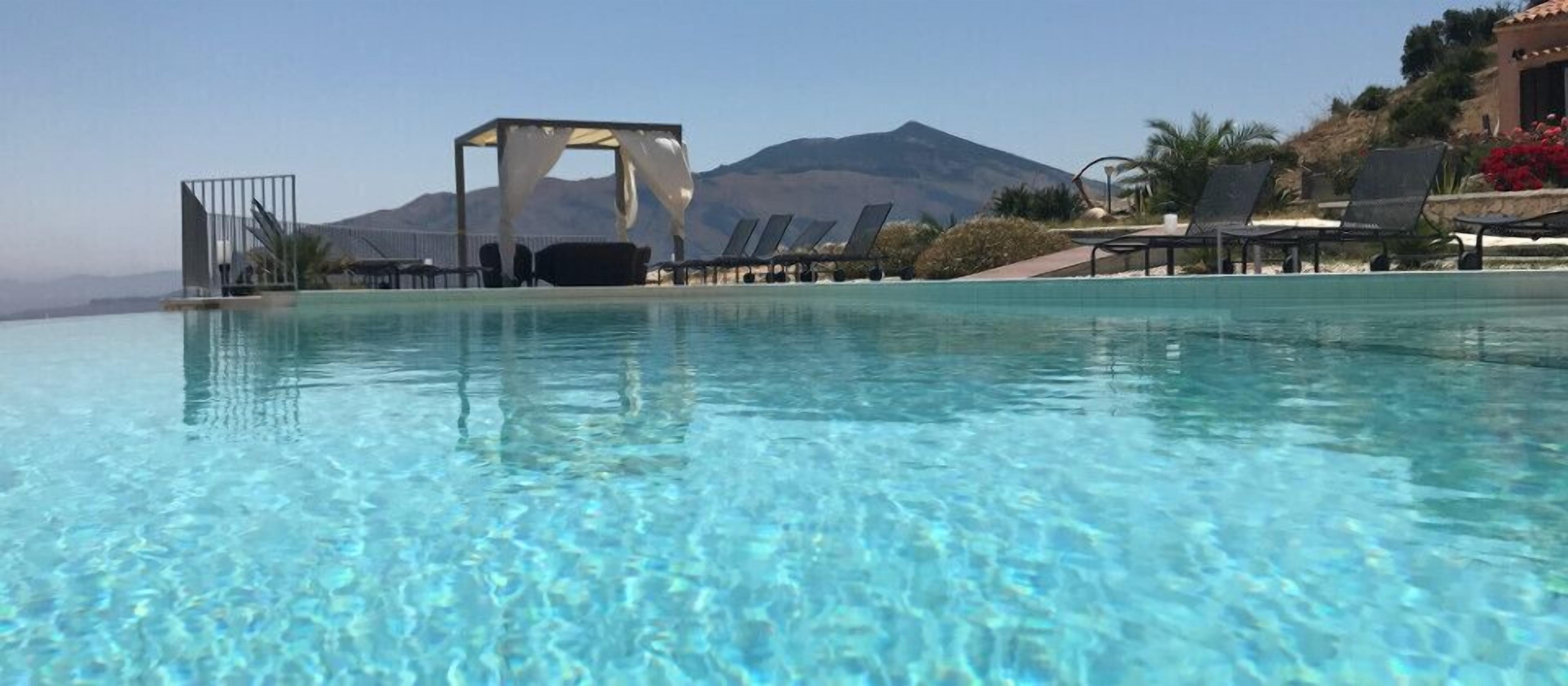 A clear pool with a mountain backdrop, lounge chairs, and a covered seating area.