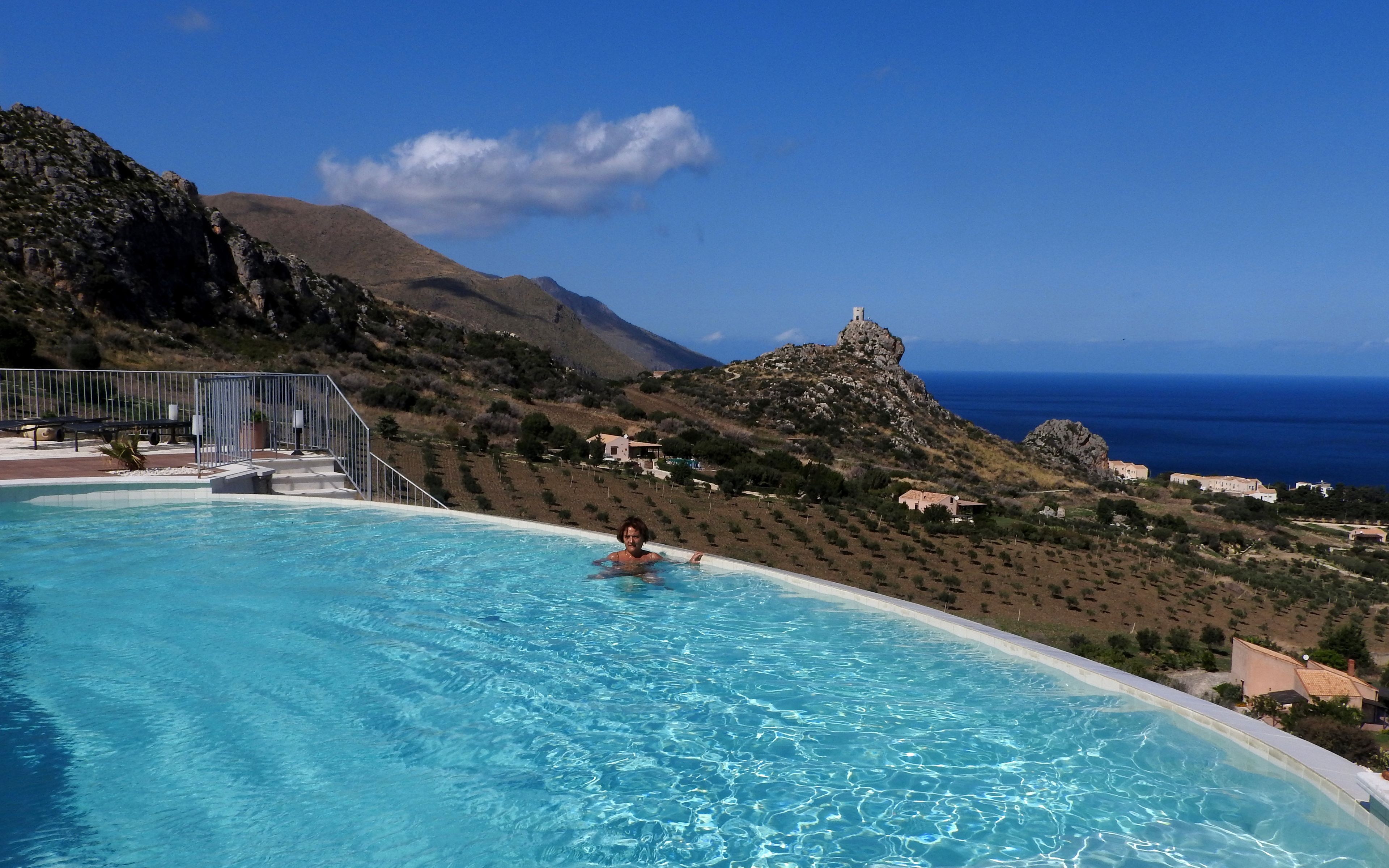 A swimming pool with a view of a mountainous landscape and the sea.