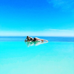 A person lying on a clear blue water surface, likely a pool, with a vast ocean and clear sky in the background. - L'Antica Cascina del Golfo (Castellammare del Golfo)