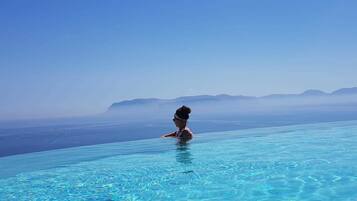 Uma pessoa à beira de uma piscina azul cristalina com vista para montanhas ao longe.