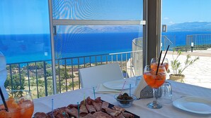 Una mesa servida con una tabla de embutidos, una copa de cóctel de naranja y vista al mar.