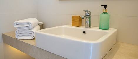 Un baño con un lavabo blanco, un jabonera de madera y un dispensador de jabón verde.