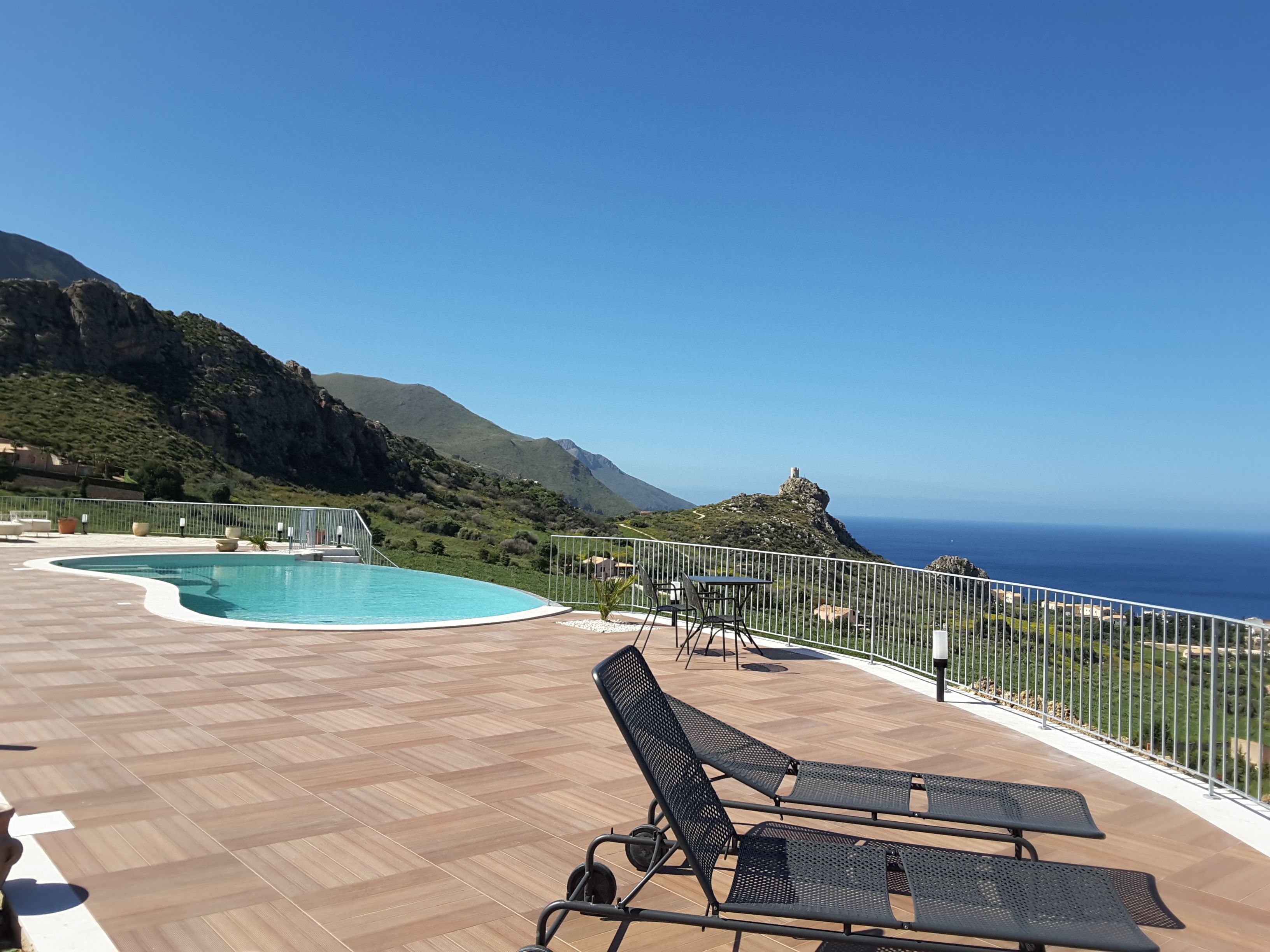Ein Poolbereich mit Liegestühlen und Blick auf das Meer und die Berge.