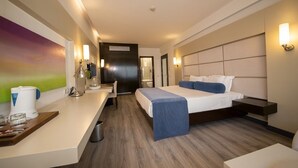 Habitación de hotel moderna con una cama, mesita de noche y escritorio con silla. Hay un cuadro en la pared y una ventana con cortinas.
