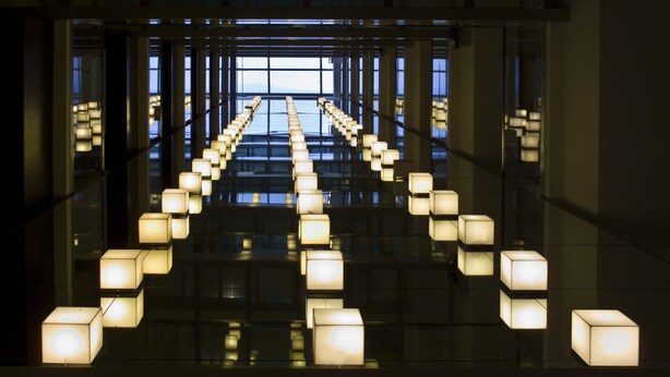 Un interior moderno con un suelo reflectante y una serie de lámparas cuadradas dispuestas en un patrón simétrico.