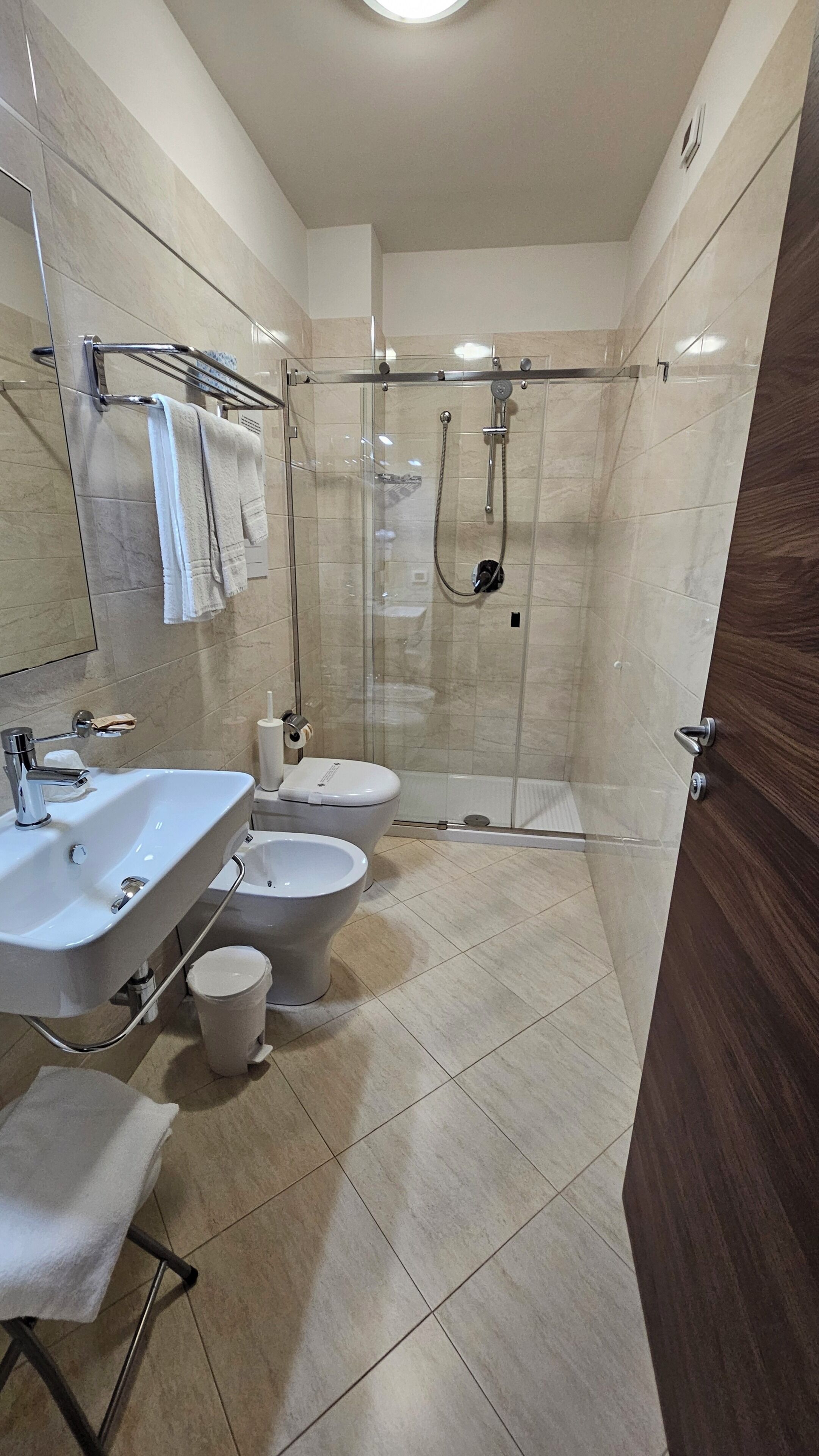 Un baño moderno con ducha envuelta en vidrio, un lavamanos, inodoro y un bidé.