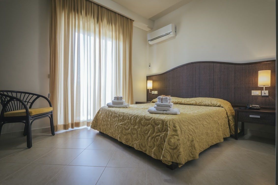 A hotel room with a large bed, a chair, a desk, and a window with curtains.