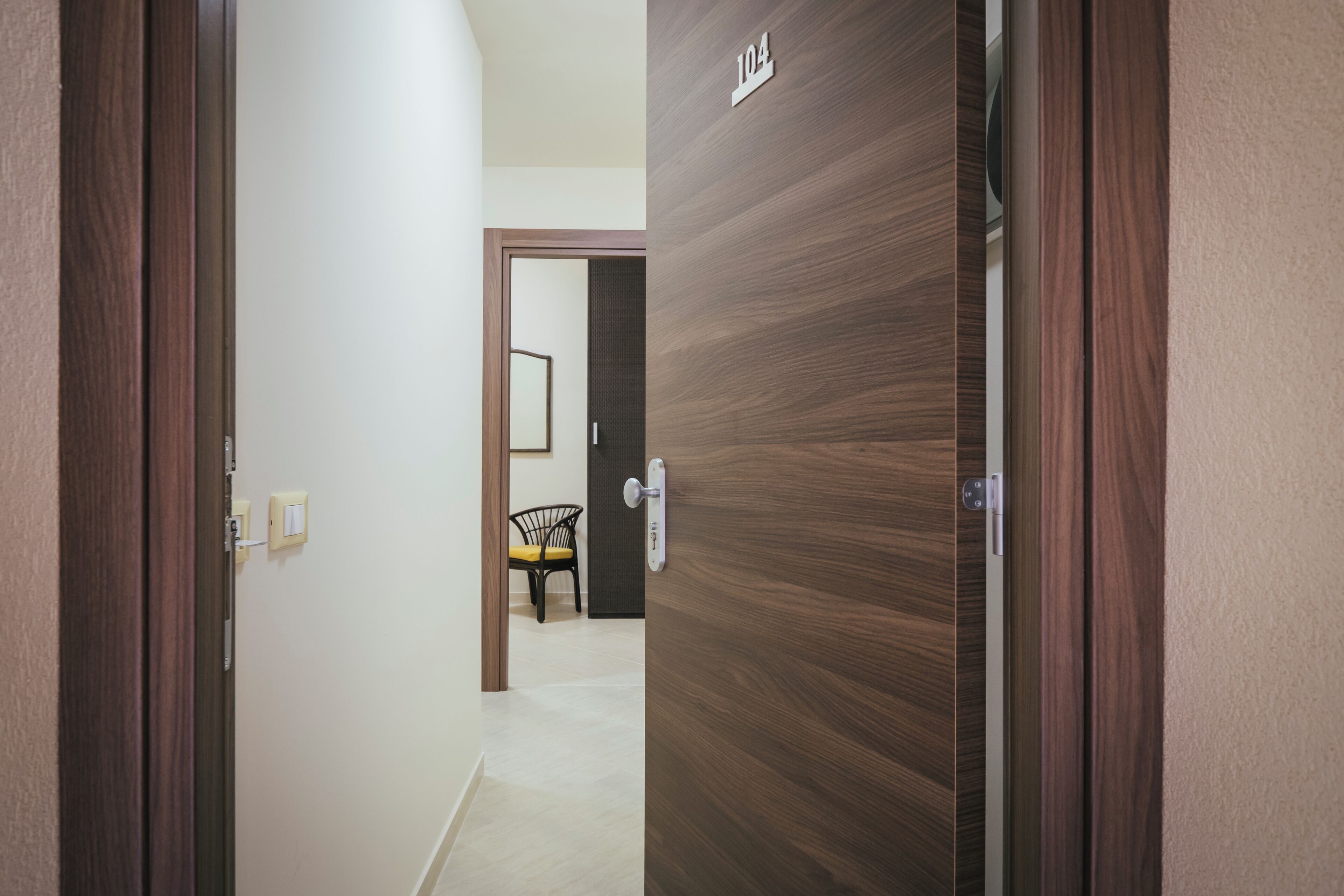 A hallway with a wooden door labeled "104" leading to a room with a chair and a small table.