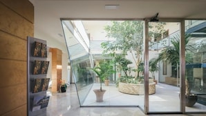 Un vestíbulo moderno con un muro de cristal, una planta en maceta y un mostrador de recepción con folletos.