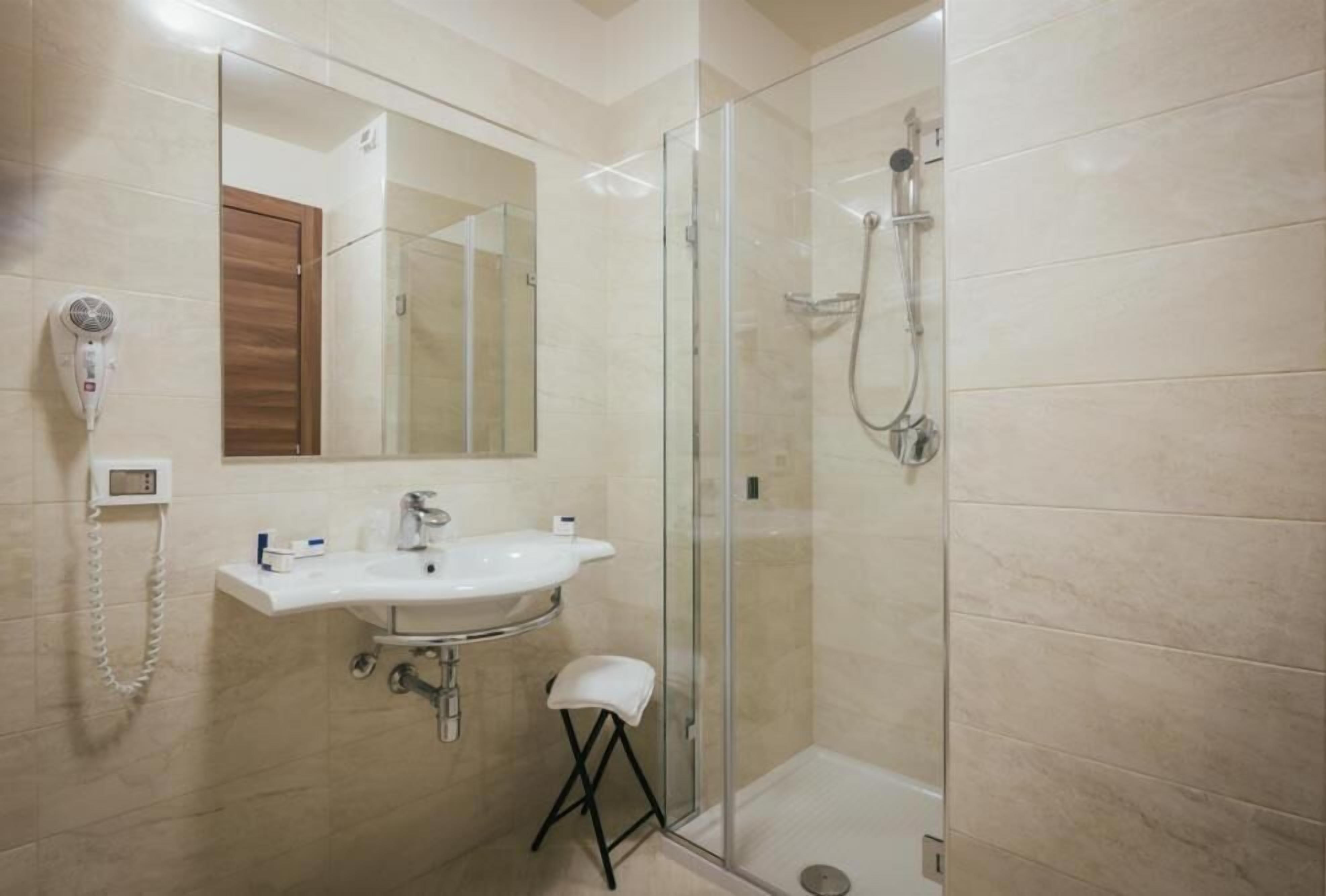 A modern bathroom with a glass-enclosed shower, a white sink, and a hairdryer on the wall.
