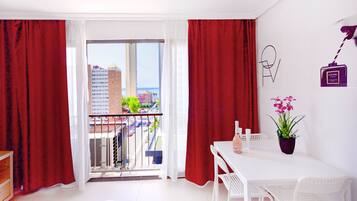 Een kamer met balkon, witte meubels, een potplant en een object aan de muur.