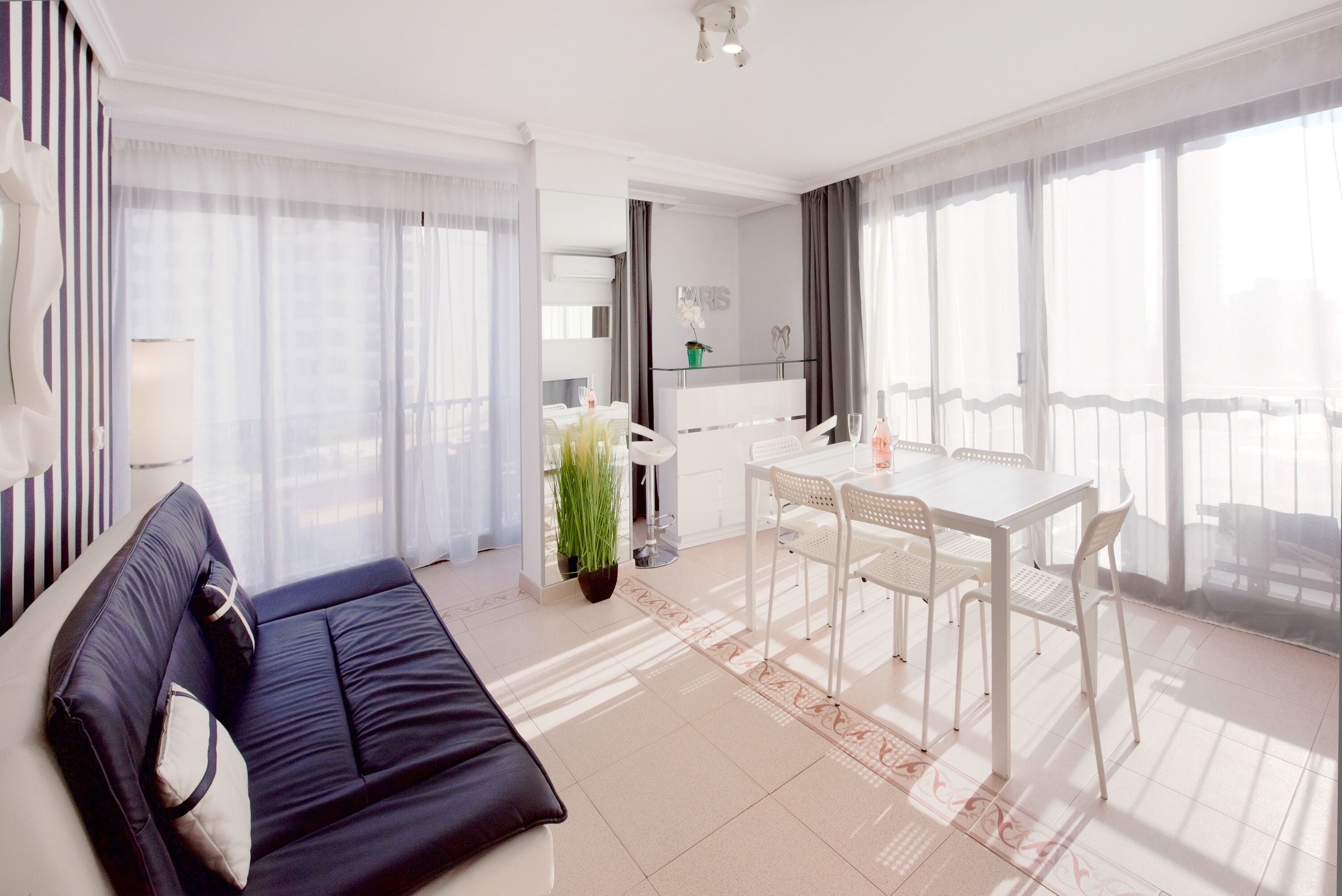 A modern hotel room with a sofa, dining table, chairs, and a potted plant.