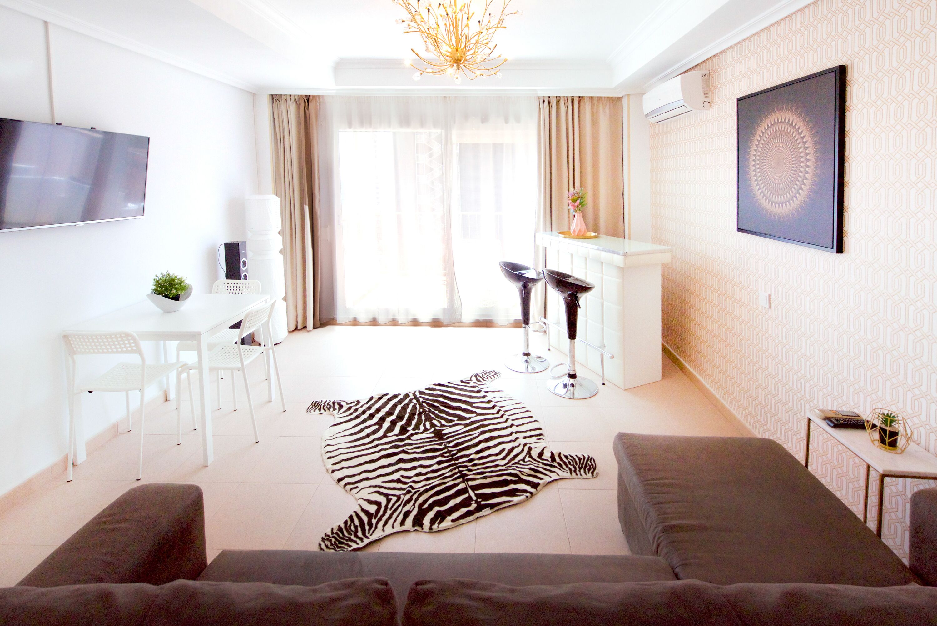 A modern living room with a zebra print rug, a sofa, a TV, a dining area with chairs, and a small table with a plant.
