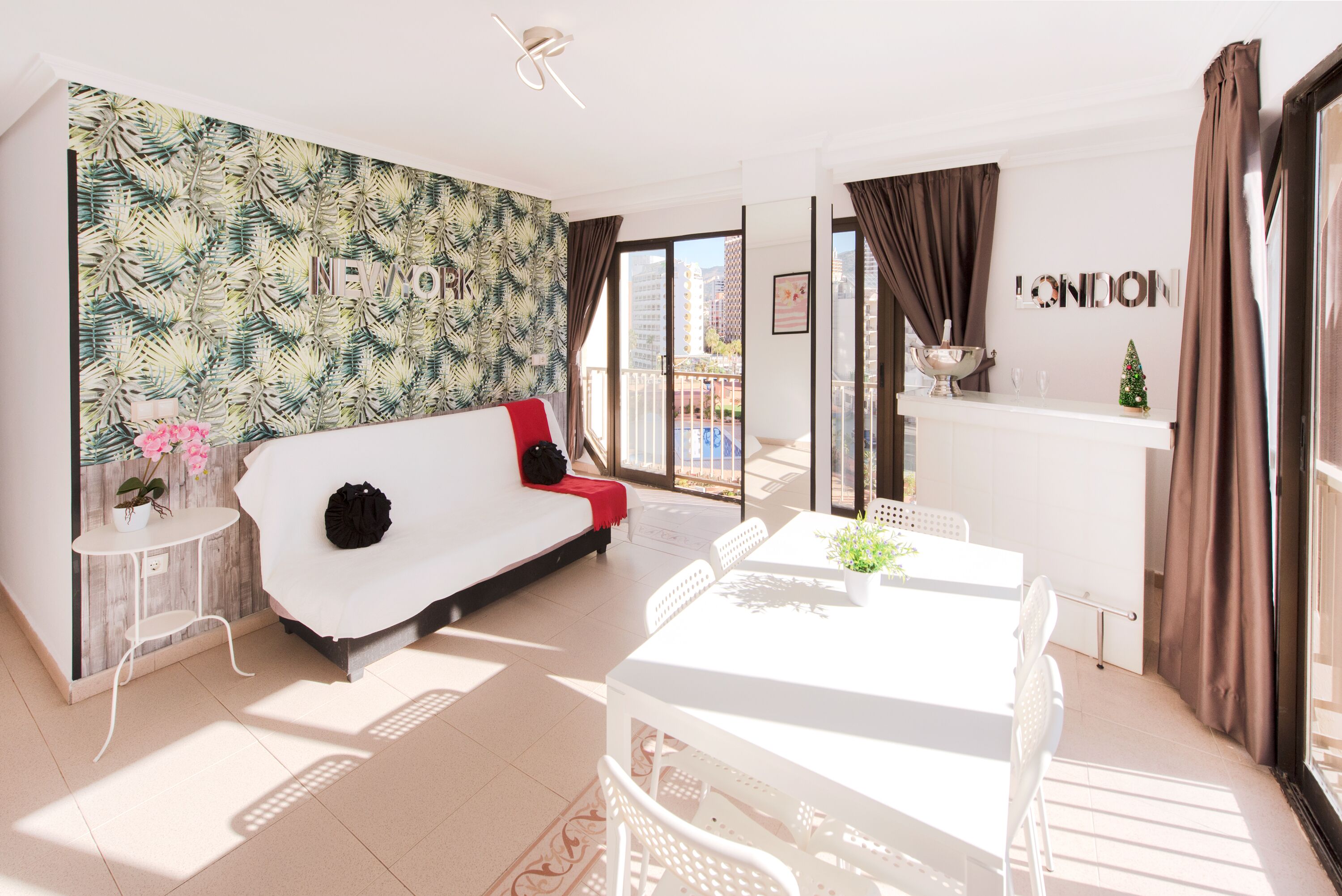 Een moderne woonkamer met een witte bank, een eettafel en een balkon met uitzicht op gebouwen.
