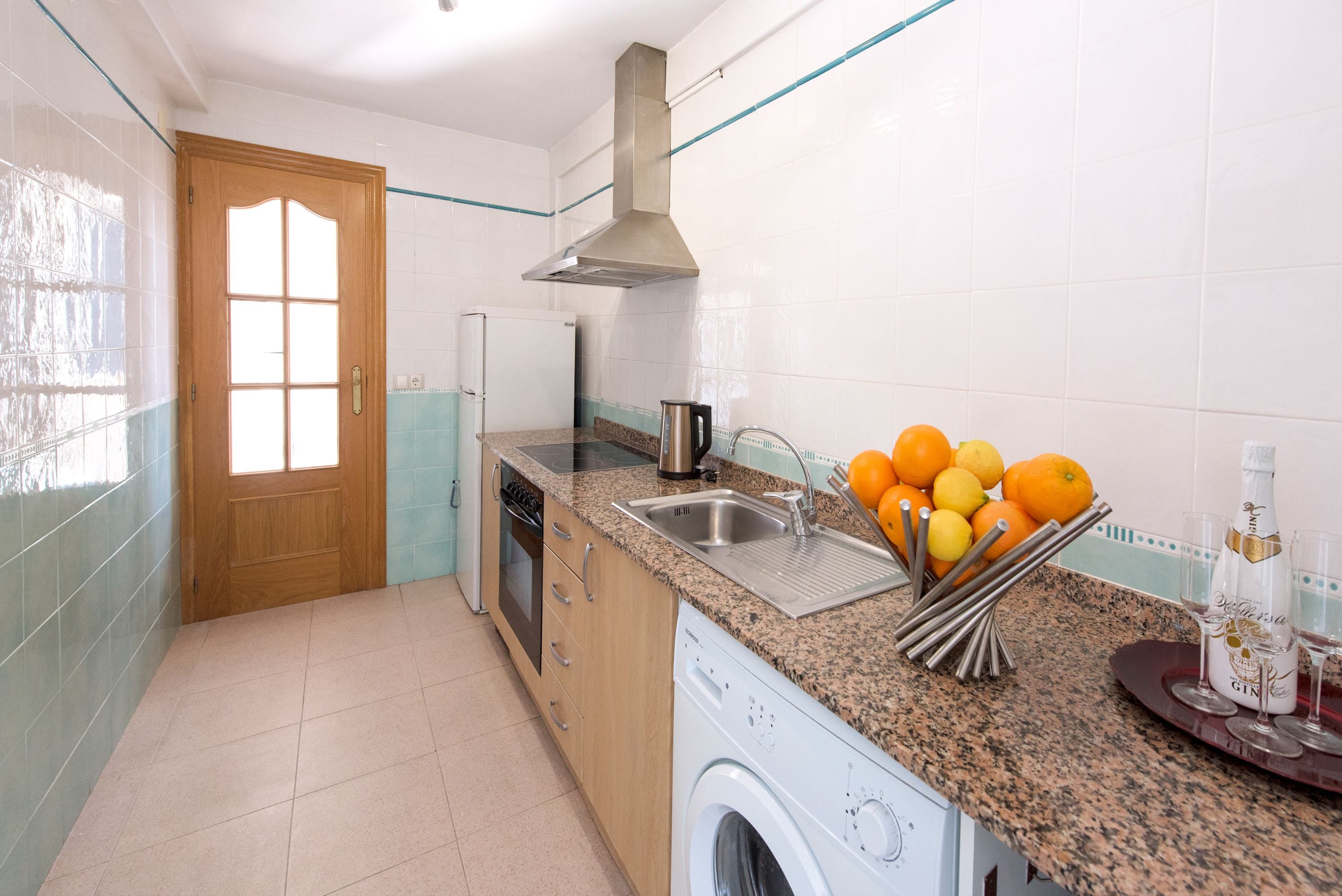 A kitchen with a washing machine, sink, and countertop with oranges and lemons.