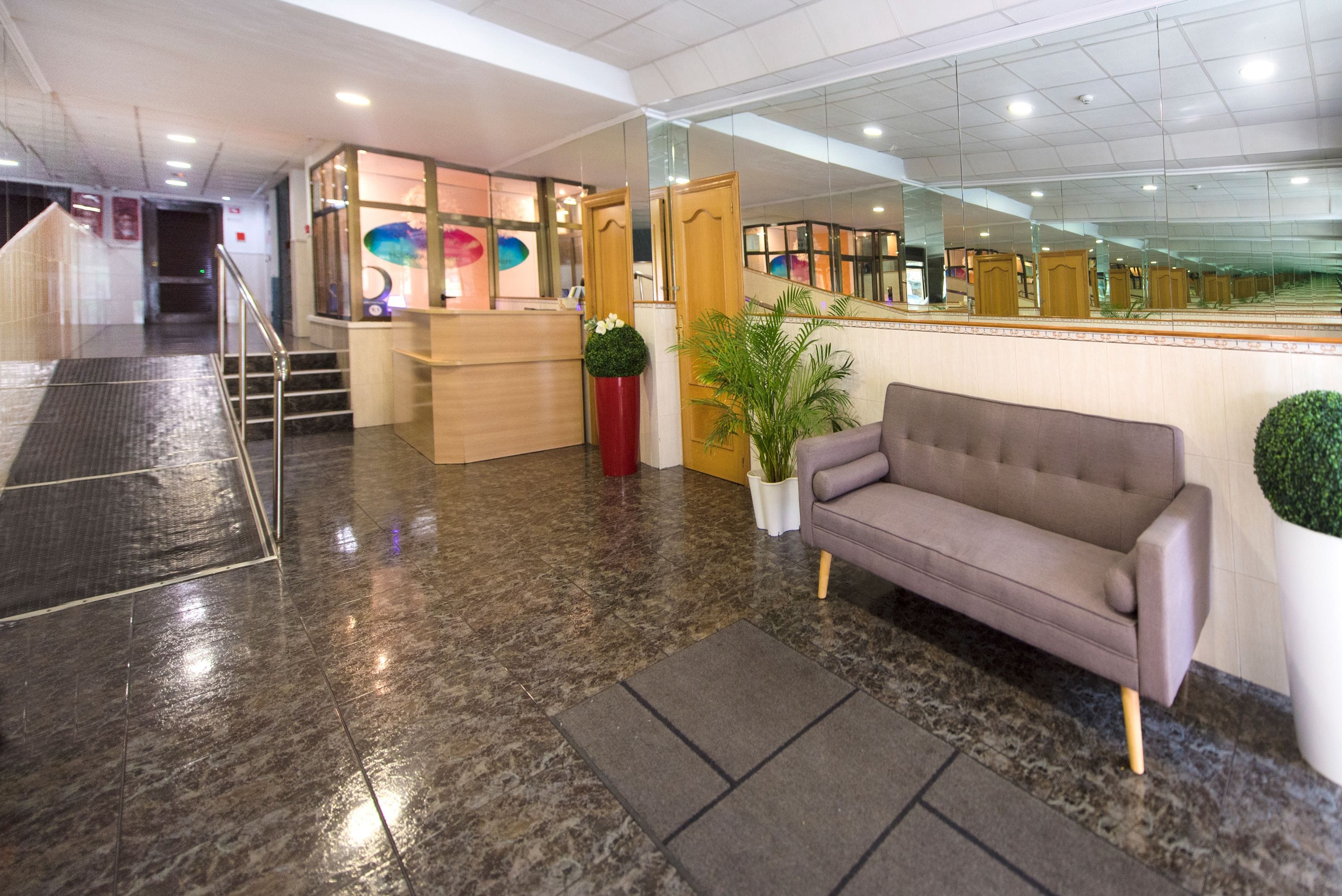 Un hall con mostrador de recepción, un sofá, una escalera y un espejo grande.