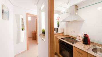 A modern kitchen with a stove, microwave, and sink. There is a potted plant on the counter and a red kettle.