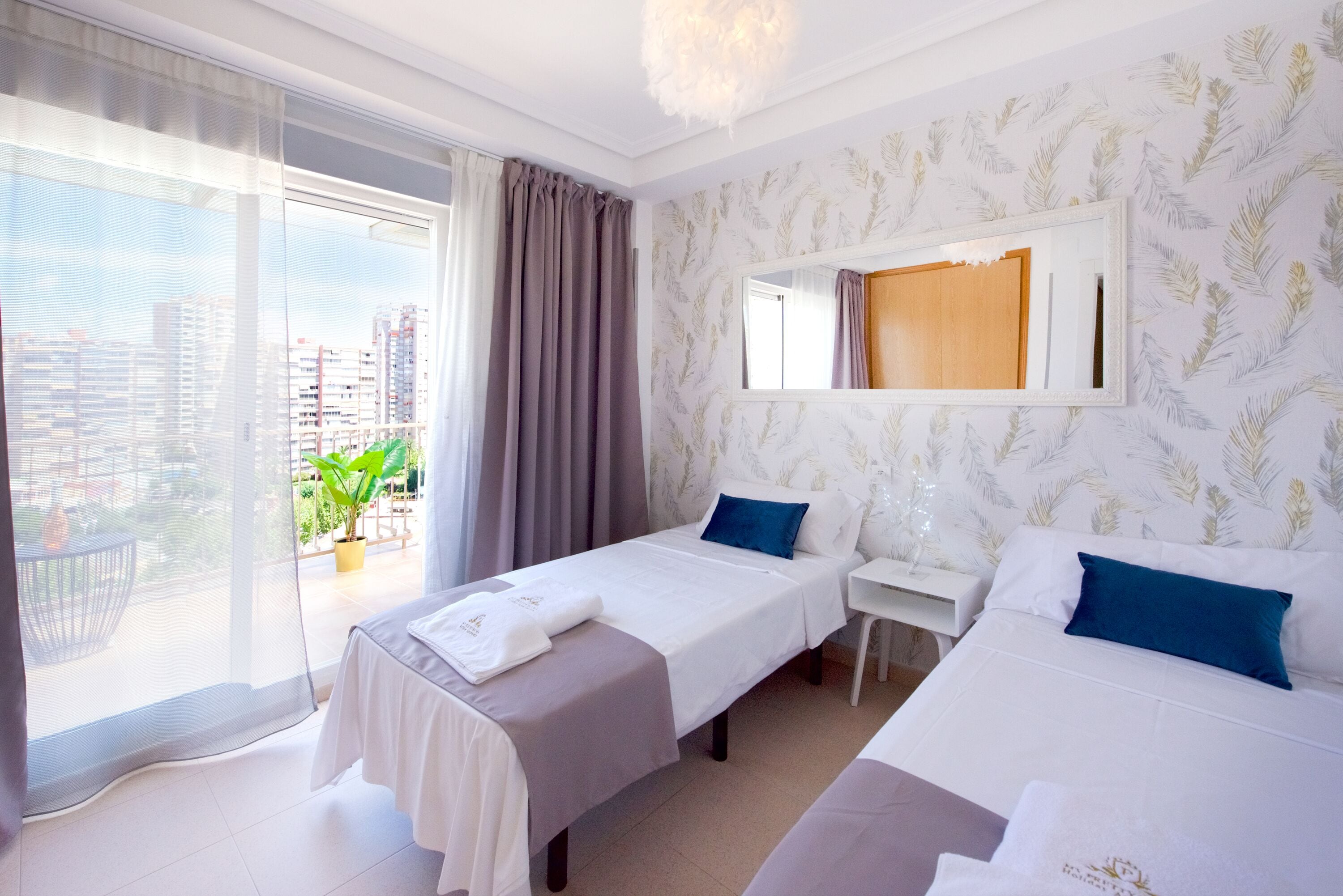A hotel room with two beds, a desk, and a large window with a view of buildings.