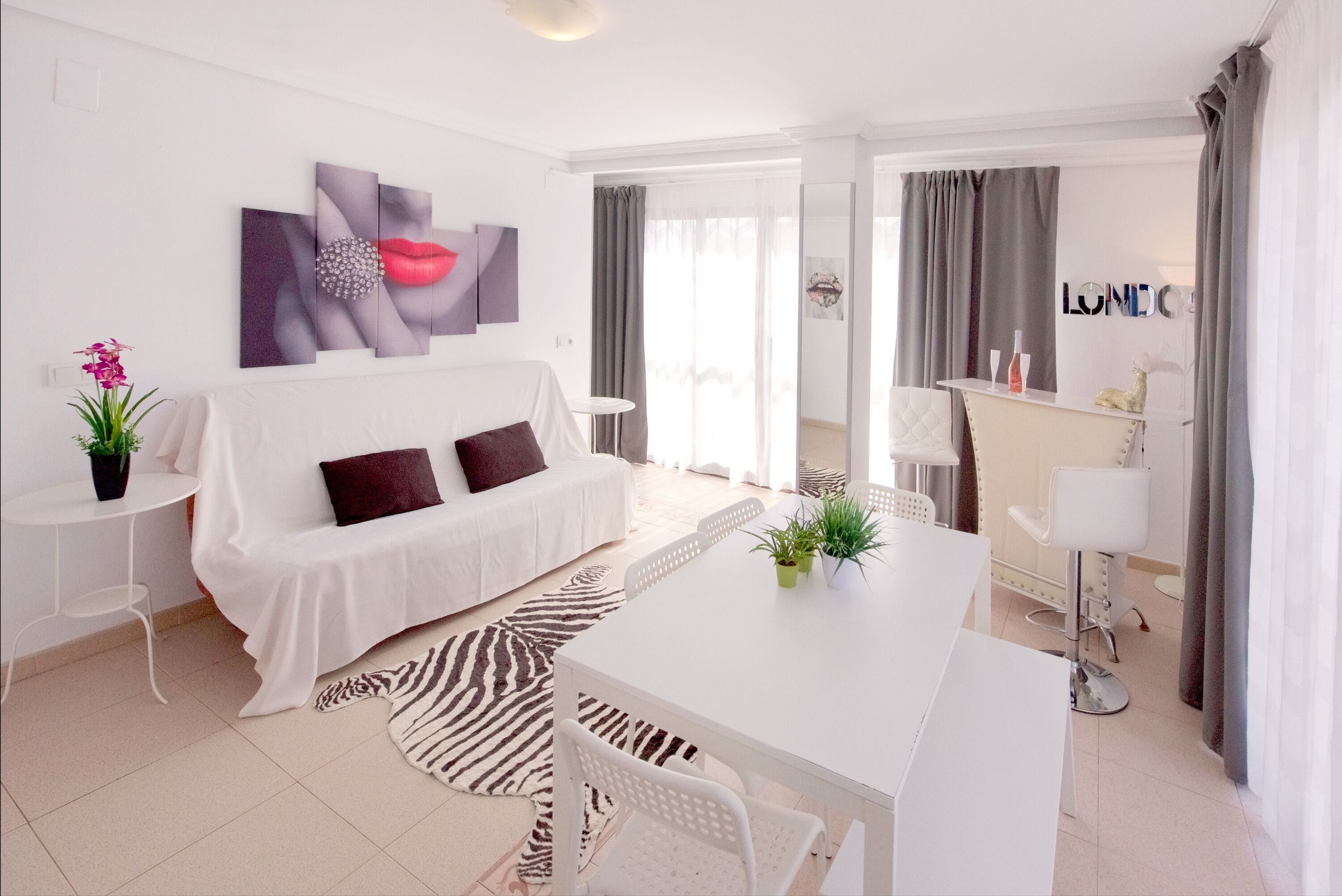 Una sala de estar moderna con un sofá blanco, un tapete estampado de cebra, una mesa de comedor con sillas y un espejo grande.