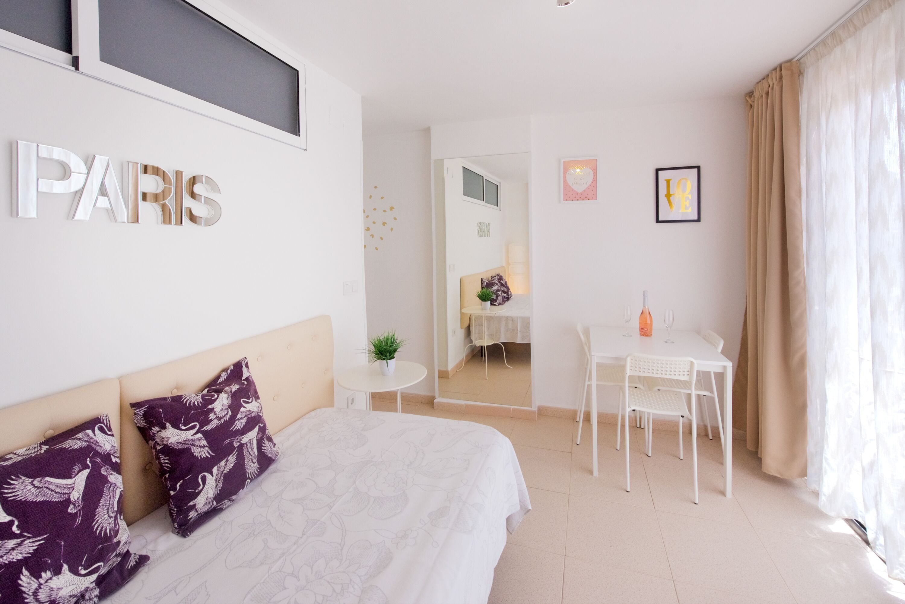 Une chambre d’hôtel avec un lit, un bureau et une chaise. Il y a une pancarte sur le mur où l’on peut lire « PARIS ».