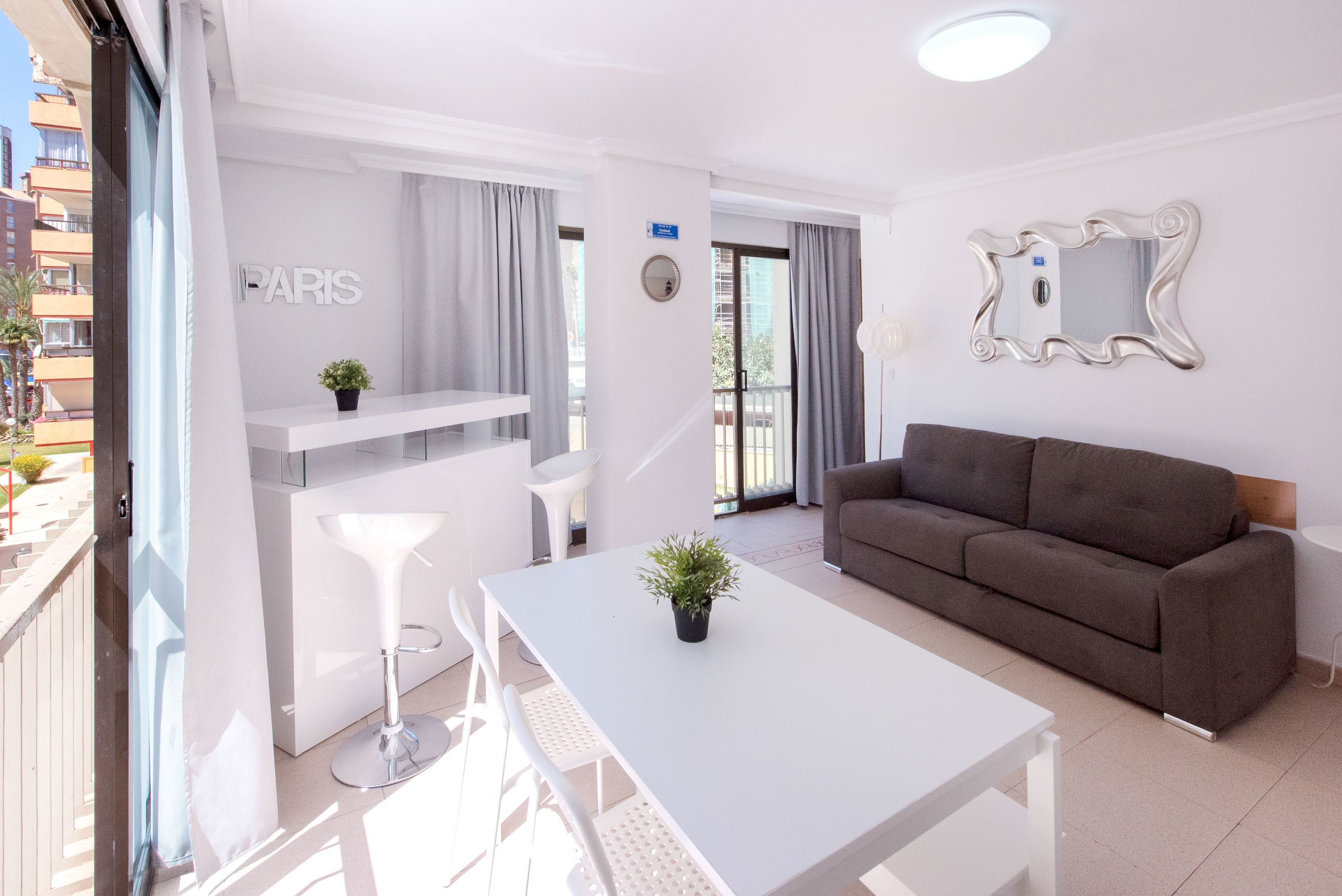 A modern living room with a white table, a brown sofa, and a balcony with a view of the city.