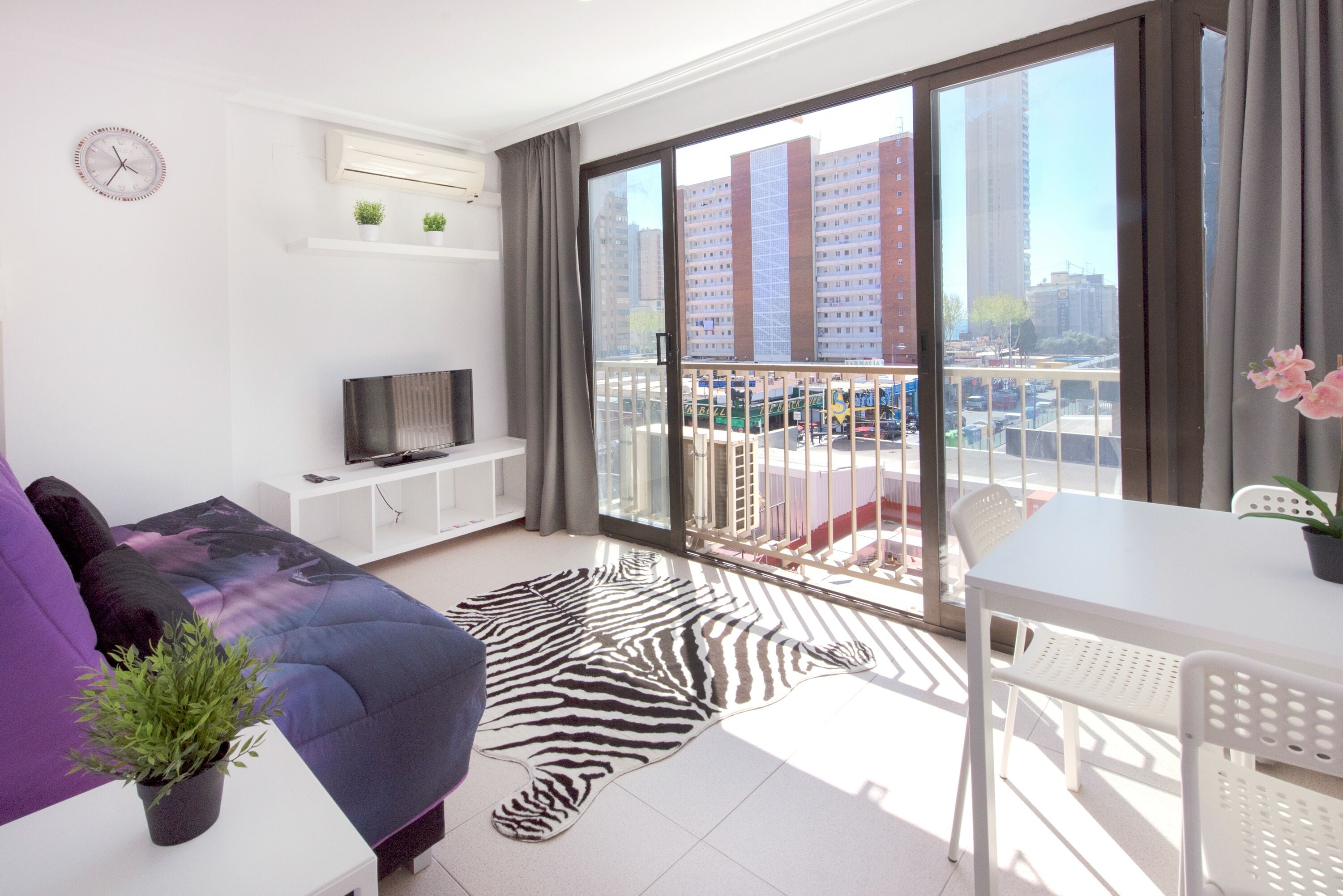 A modern living room with a sofa, TV, and balcony with a view of the city.