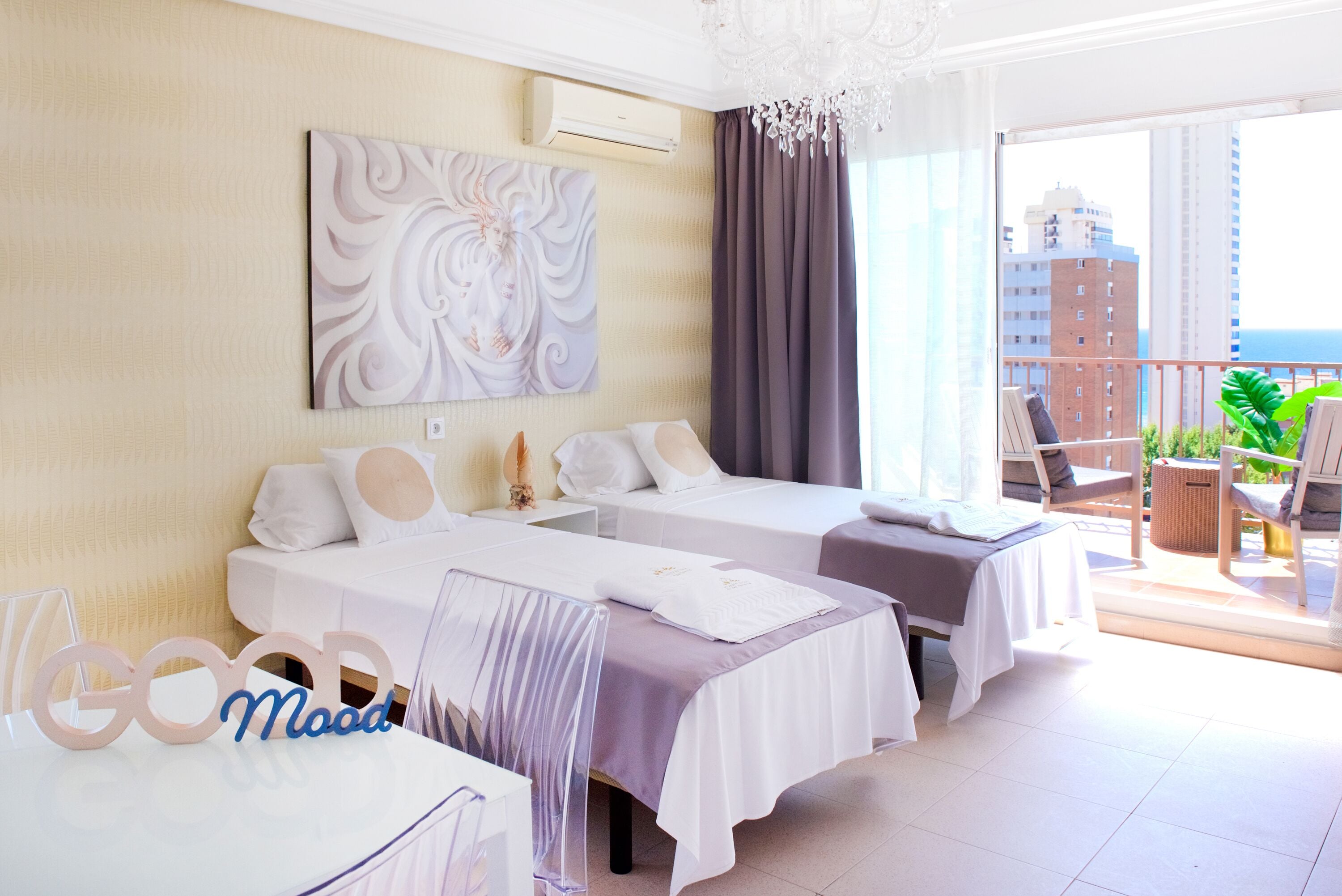 Une chambre d’hôtel avec deux lits, un balcon offrant une vue agréable et une grande peinture abstraite accrochée au mur.