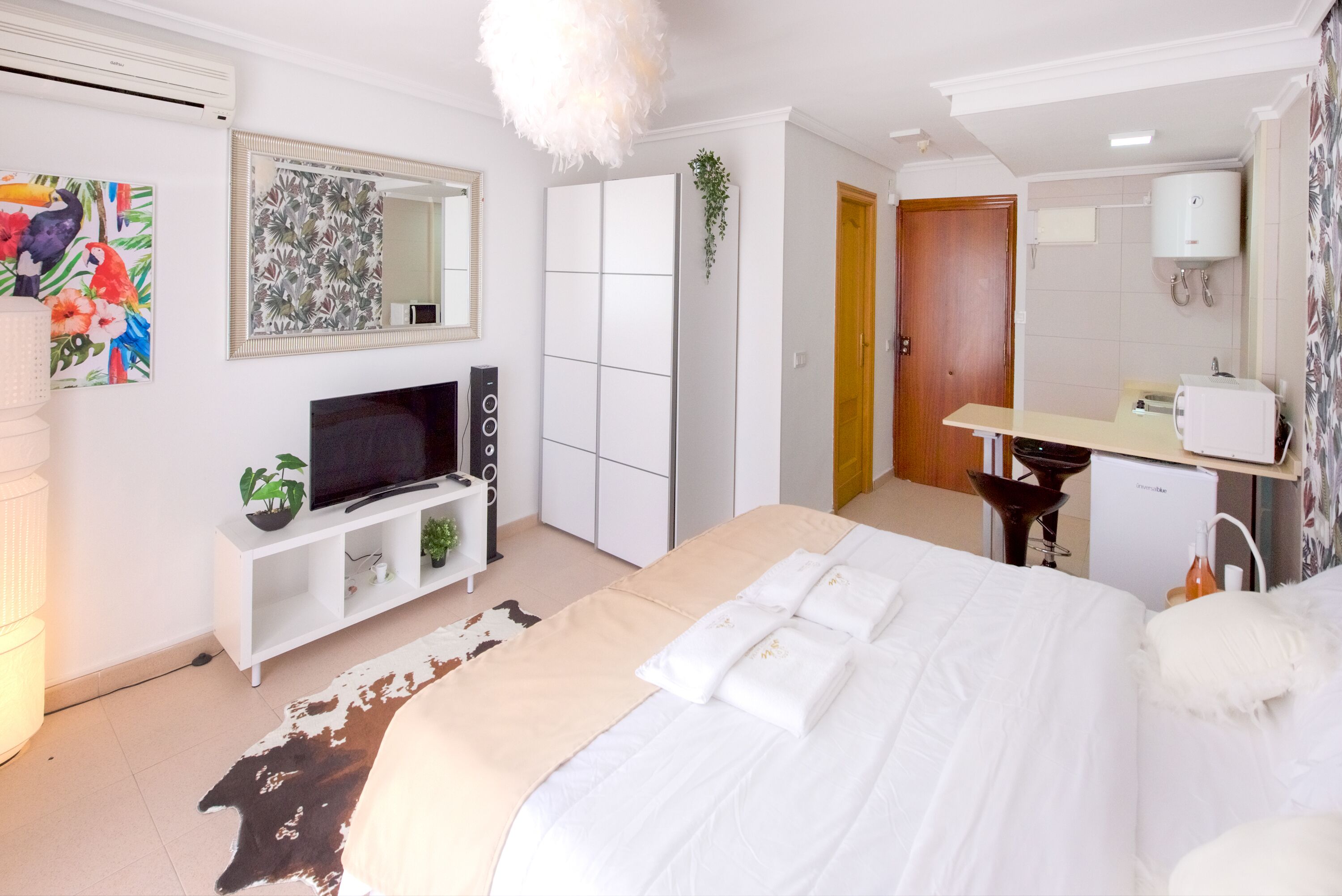 A hotel room with a bed, a TV, a wardrobe, a mirror, and a bathroom with a sink and toilet.