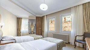 Habitación de hotel con dos camas, un escritorio de madera, una silla y vista a un edificio histórico por la ventana.