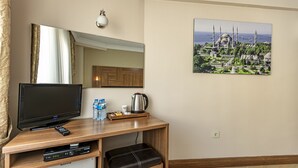 Habitación de hotel con un escritorio de madera, un televisor de pantalla plana, un control remoto, una tetera, agua embotellada y una taza de café.