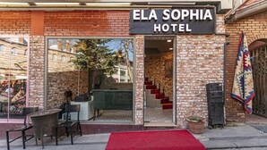 La entrada del HOTEL ELA SOPHIA, con una alfombra roja, fachada de ladrillo y una escalera que da a su interior.