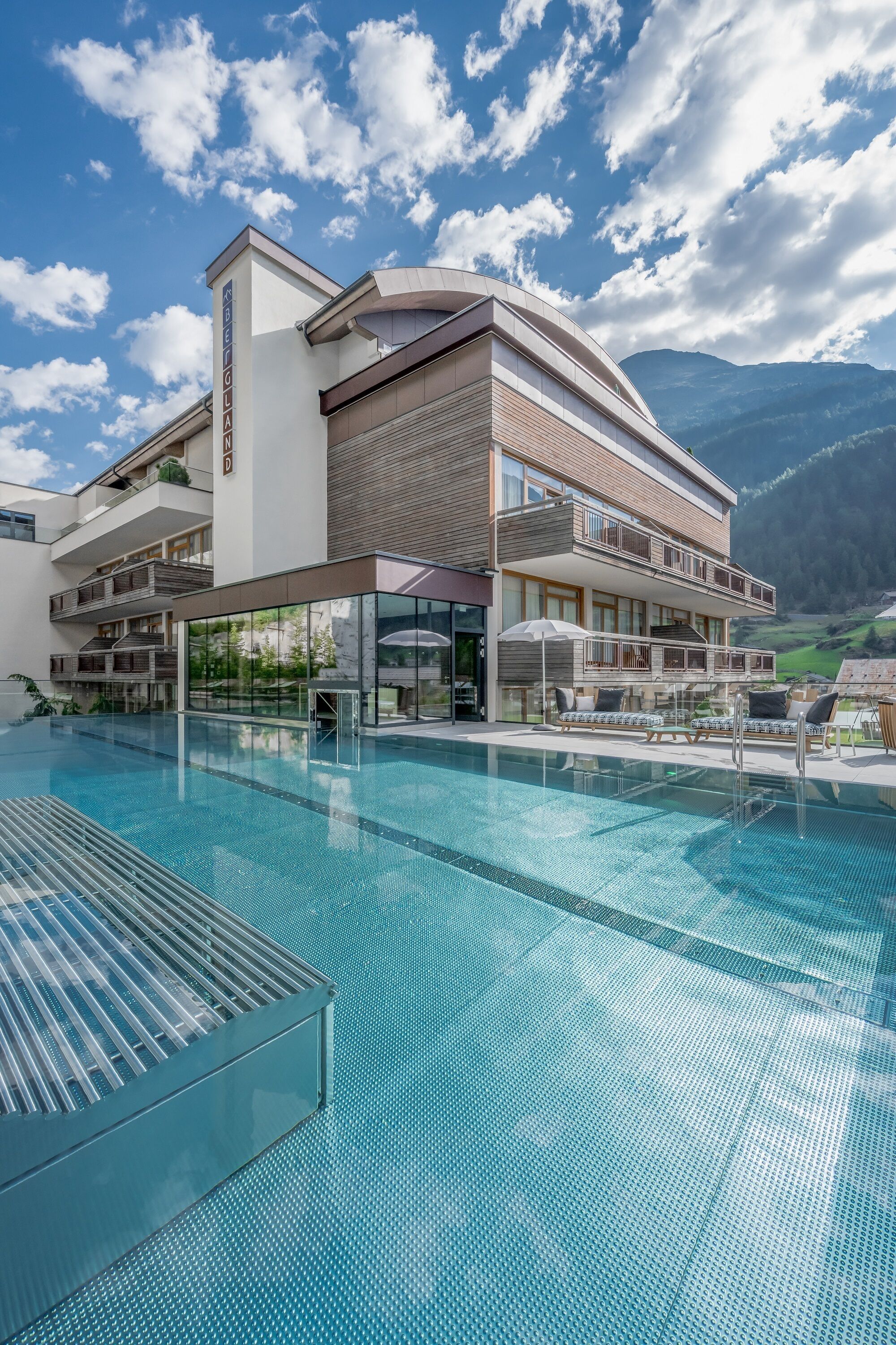 A modern hotel with a pool, a second-story balcony, and mountain views.
