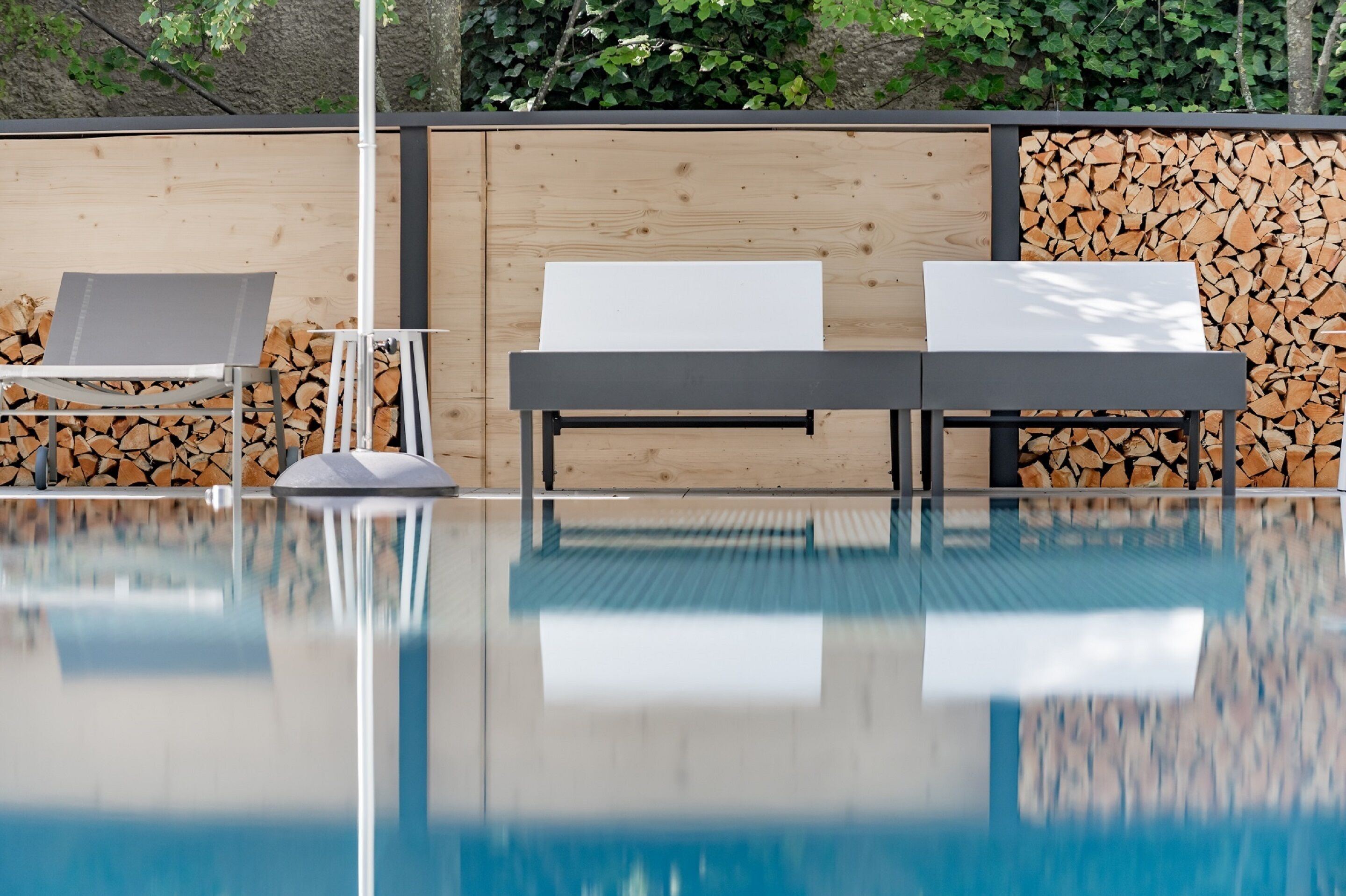 Un área de piscina con dos sillas de descanso y una mesa, rodeada de paredes de madera y una pila de leña.