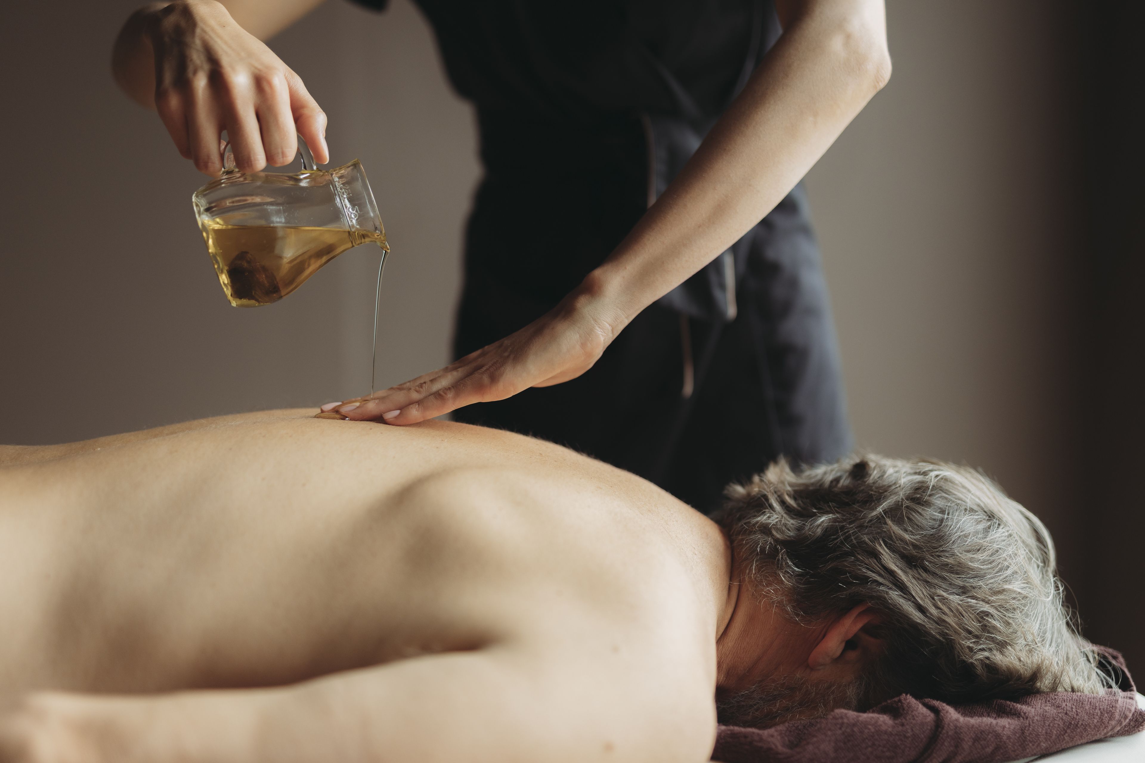 A person receiving a back massage with oil being poured on them.
