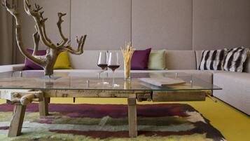 Un salon moderne avec une table basse en verre, une branche d’arbre décorative, deux verres à vin et un tapis coloré.