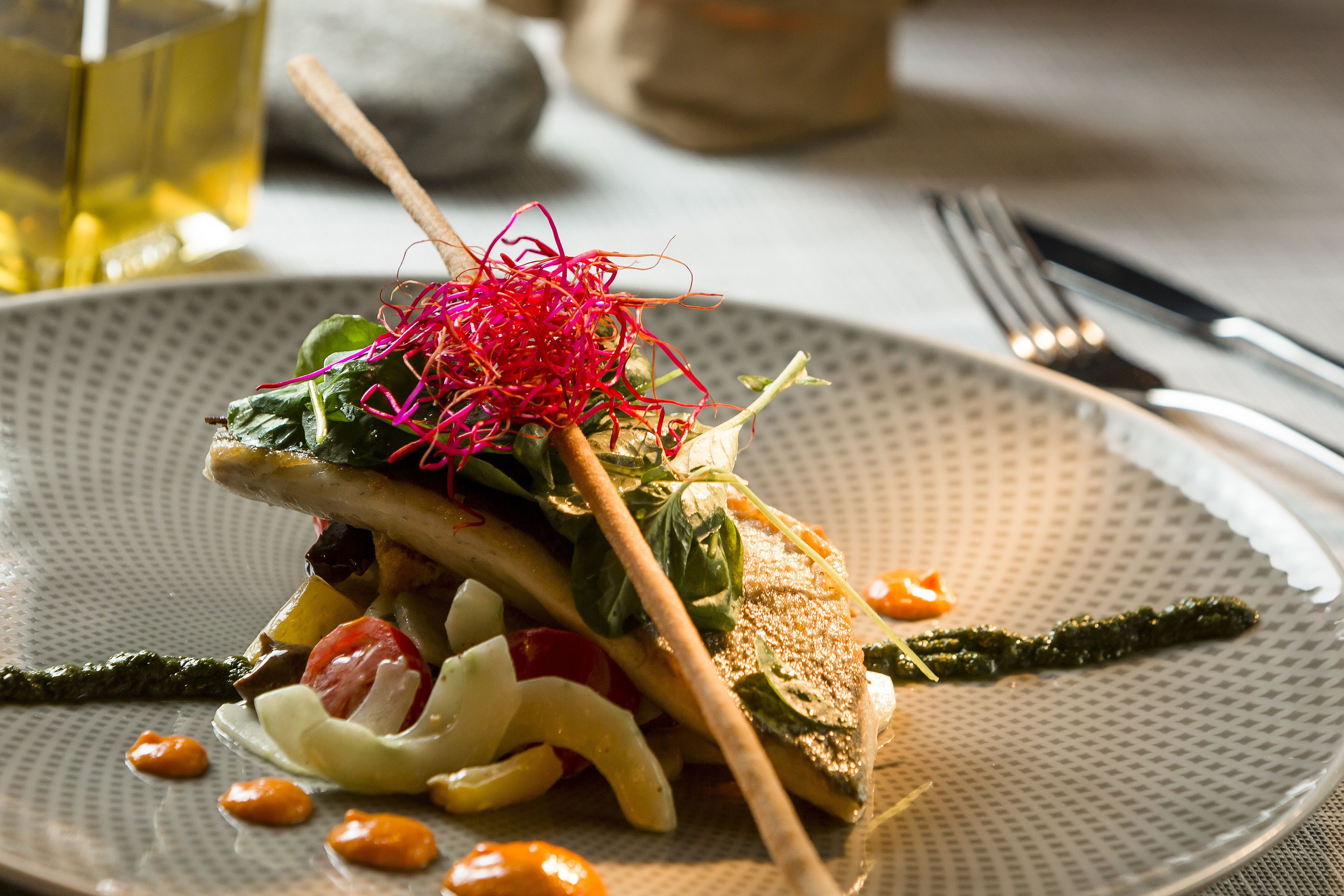 A plate with a fish fillet, vegetables, and a decorative garnish.