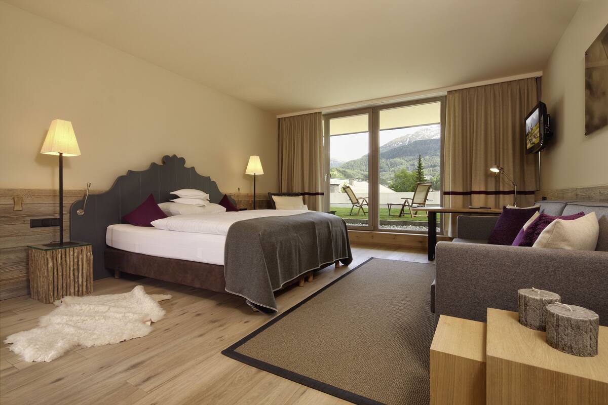 A hotel room with a bed, a sofa, a view of the outdoors, and a television on the wall.