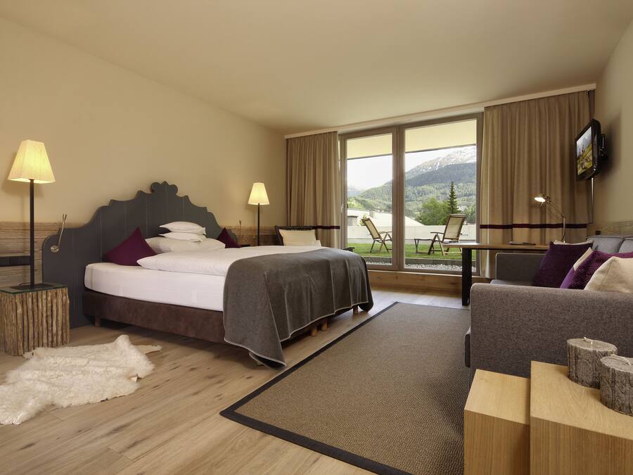 Ein Hotelzimmer mit einem Bett, einer Couch, Blick ins Freie und einem Fernseher an der Wand.