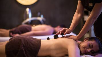 Eine Massagebehandlung, wobei eine Person liegend mit dem Gesicht nach unten auf einer Liege eine Rückenmassage erhält.