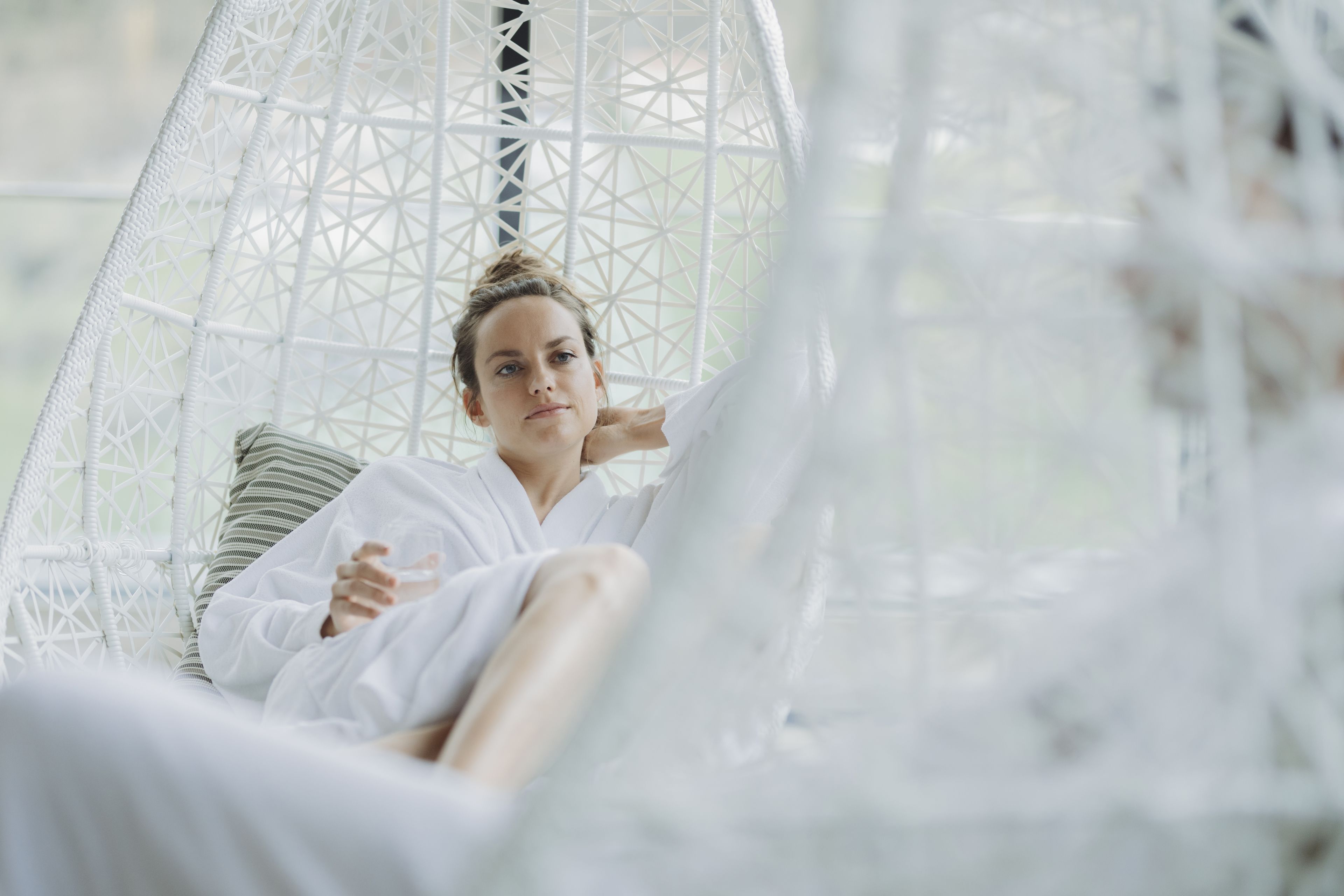 A person in a white, geometric-patterned hanging chair with a striped pillow, in a room with a light, airy feel.