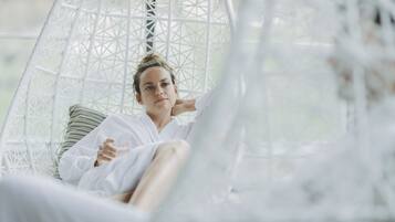 A person in a white, geometric-patterned hanging chair with a striped pillow, in a room with a light, airy feel.