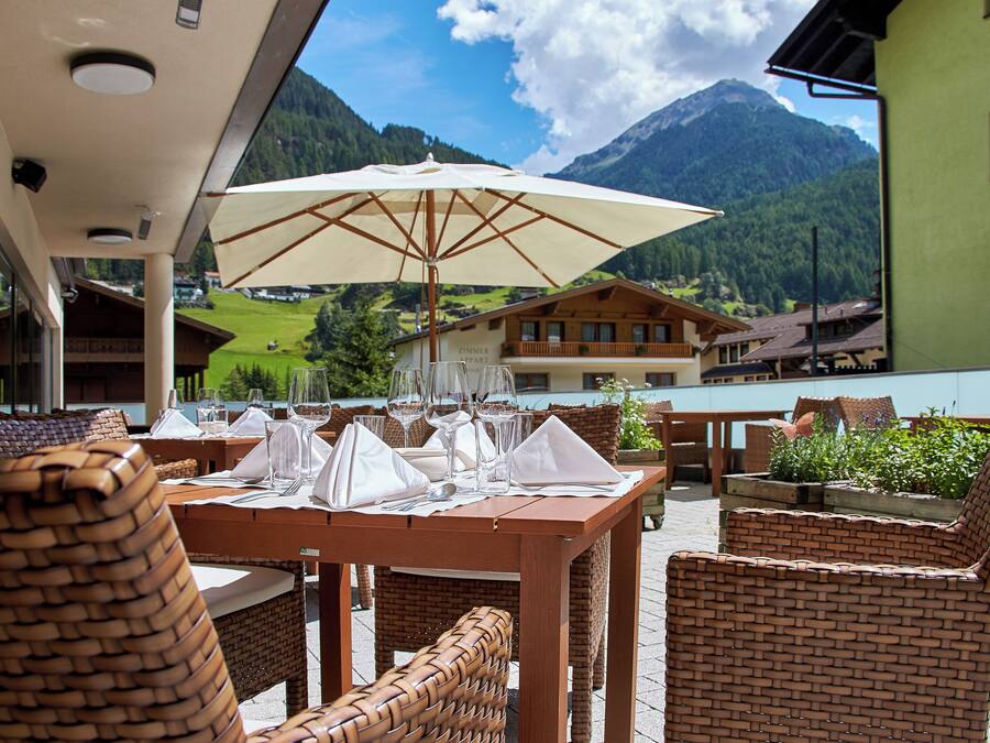 A dining area with wicker furniture, a table set for a meal, and a mountain view in the background.