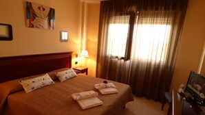 A hotel room with a large bed, a nightstand with a lamp, a desk with a computer, and a window with curtains. - Fidenza Hotel (Fidenza)