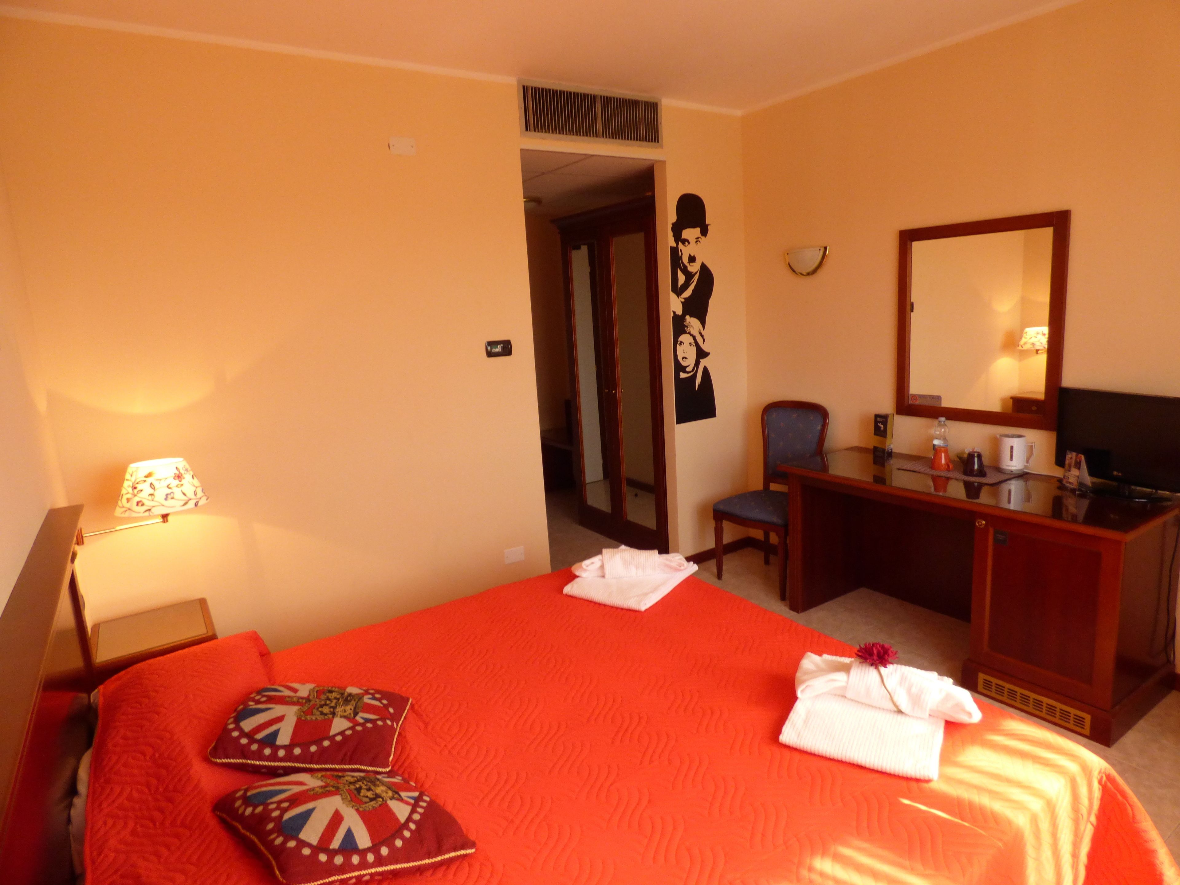 Una camera d'albergo con un letto, una scrivania, una sedia, una televisione e uno specchio.