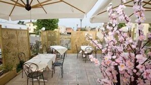 An outdoor patio area with tables and chairs, covered by a large umbrella, and a decorative plant in the foreground. - Fidenza Hotel (Fidenza)