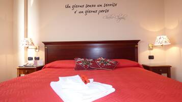 A neatly made bed with red bedding and two pillows, a bedside table with a lamp, and a wall with a motivational quote.